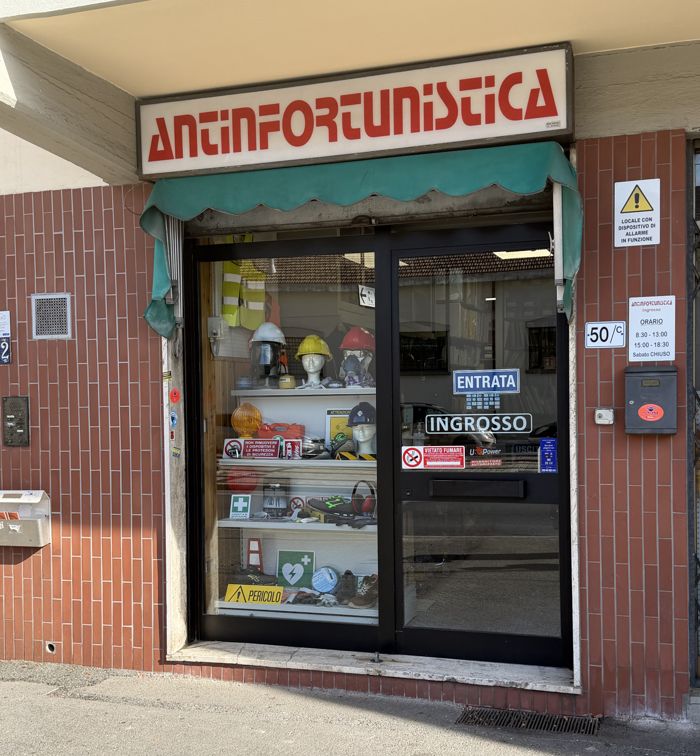 L'ingresso del negozio: insegna rossa Antinfortunistica, vetrina con caschi e cartelli, civico 50/c